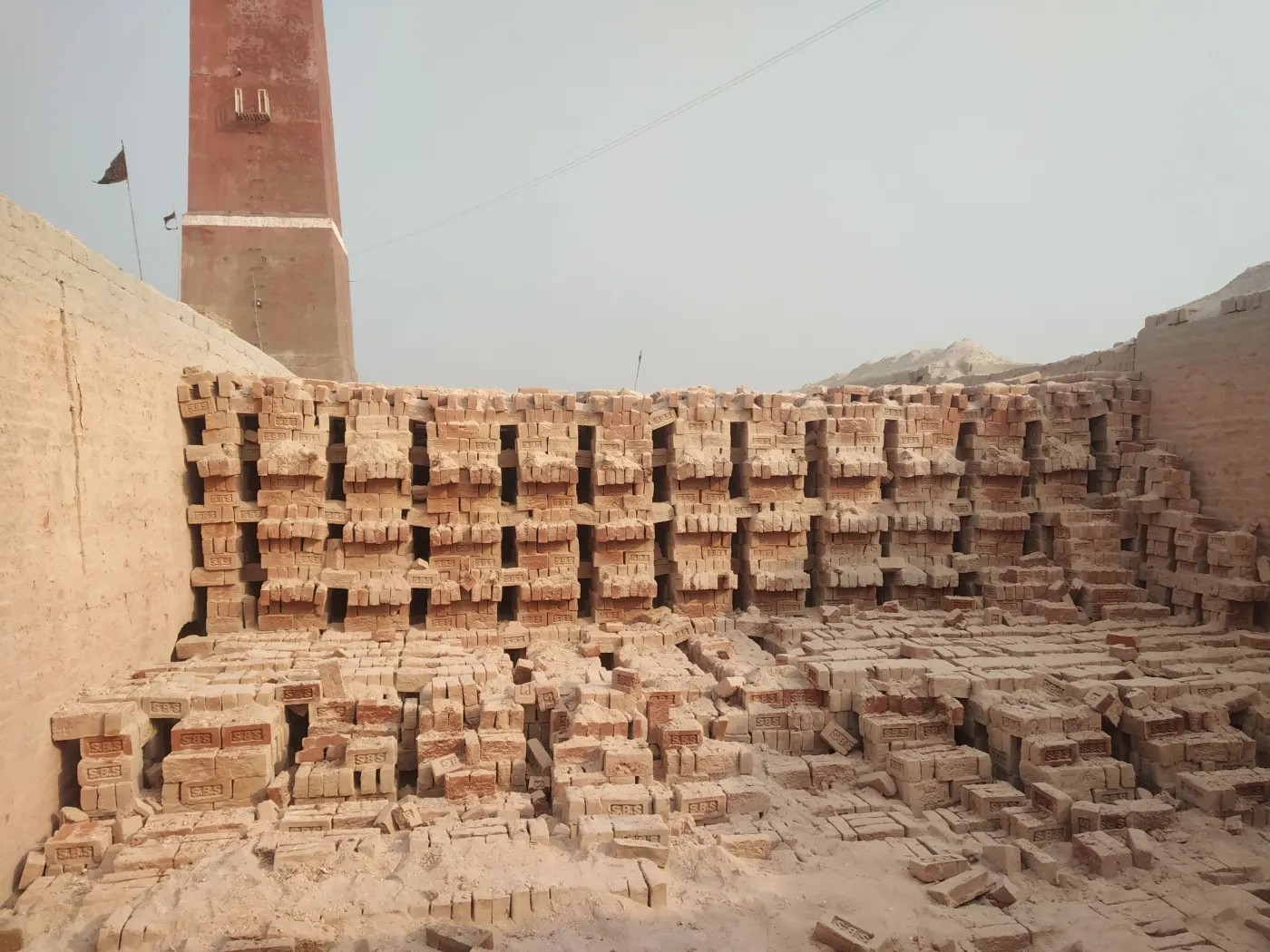 Fired bricks stacked in the yard below a kiln chimney